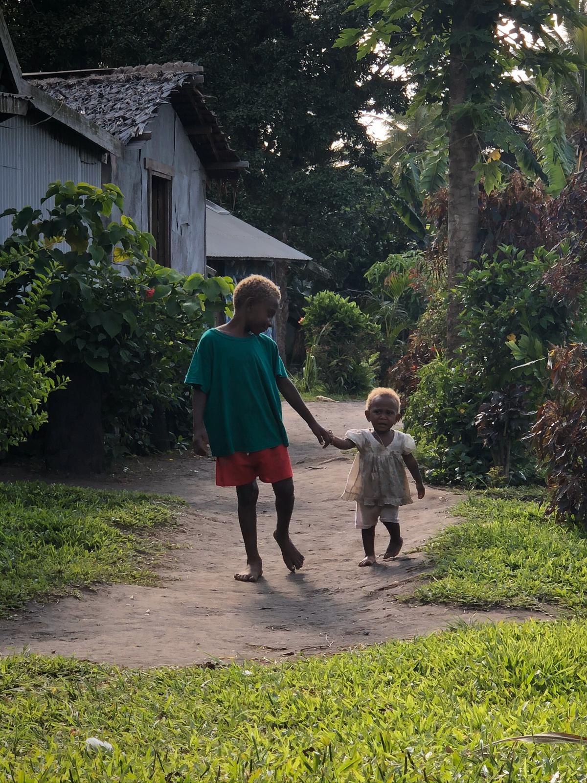 Two children walking hand in hand through a village path